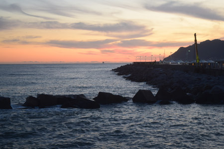 Sunset over the sea with rocks in the foreground and a lighthouse in the backgroundの写真素材