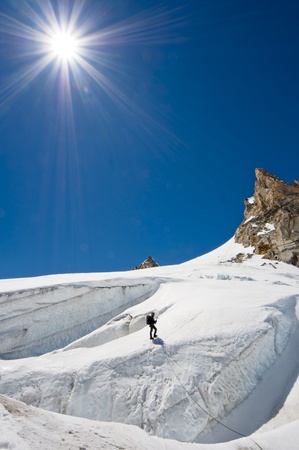 A male climber , dressed in black, climbs up a snowy slope. Winter clear sky day.の写真素材
