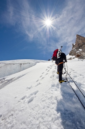 A male climber , dressed in black, climbs up a snowy slope  Winter clear sky day の写真素材