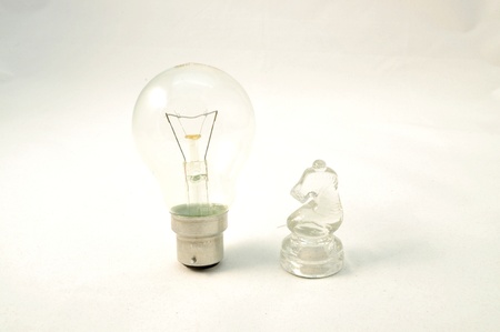 two glass objects on white background -a chess knight and an electric light bulbの写真素材