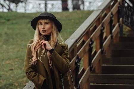 Young blonde woman wearing the black hat standing on the wooden stairs. Woman portraitの写真素材