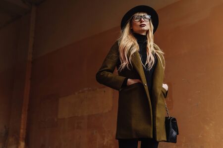 Blond woman wearing glasses and black hat and holding her hands in the coat pockets. Woman portraitの写真素材