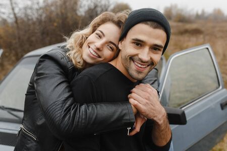 Smiling woman emracing her man from the back at the background of the car. Happy loversの写真素材