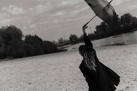 Woman in the coat walking with umbrella on the river bank. Woman portraitの写真素材