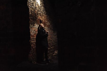 Young man standing near the wall in the abandoned buiding under light ray. Man portrait