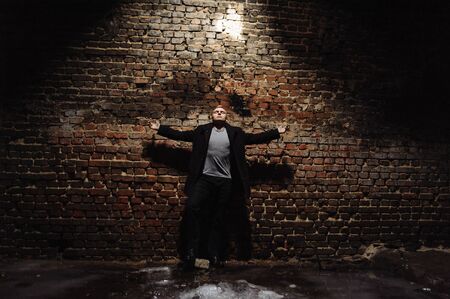 Young man in the coat standing near the wall with arms wide apart. Man portrait