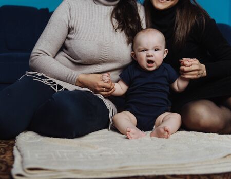 Baby yawning while sitting between mom and grandmomの写真素材