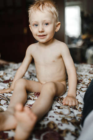 Smilling little boy sitting on the bed without t-shirt. Child portraitの写真素材
