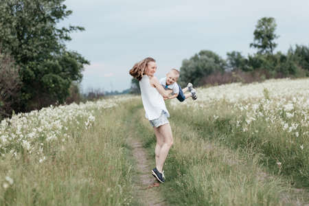 Smiling mother playing with her little son in nature. Mom holding son in the arms and doing plane. Mother and son. Happy familyの写真素材