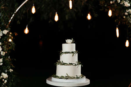 Three-tier minimalistic wedding cake at the background of the lights. Cake at the wedding