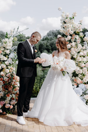 Happy groom and beautiful bride at a wedding ceremony under an arch decorated with flowers exchange rings. High quality photoの写真素材