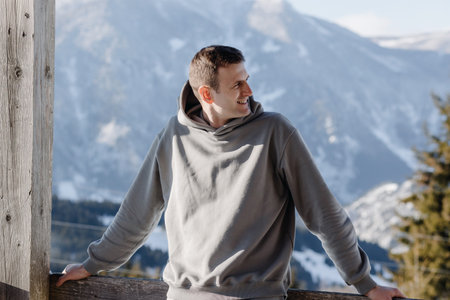 Attractive young european handsome guy looks away. Close-up portrait of a middle-aged European man in his 30s in a gray tracksuit against the backdrop of winter mountains. High quality photoの写真素材
