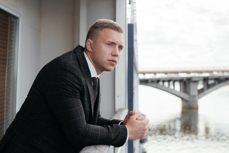 The groom in a classical clothes is standing on the balcony, looking away.