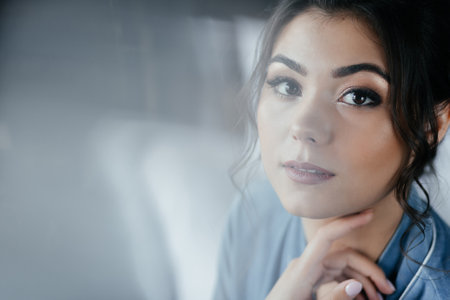 The bride in a blue robe sits on the bed and looks at the camera. Close up