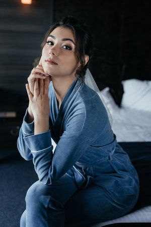 The bride in a blue robe sits on the bed and poses for the cameraの写真素材
