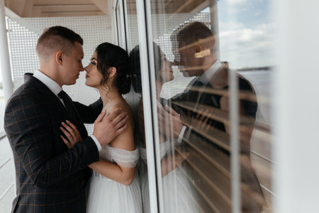 Romantic groom kissing brunette bride in the neck near an old window, mirror reflectionの写真素材