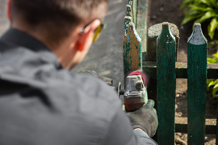 Sanding and preparing a wooden fence for painting. The master is restoring near the house. Close up