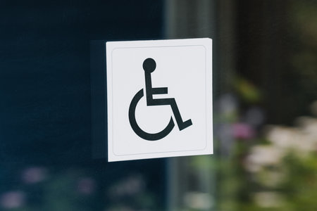 Black sign for people with disabilities in a wheelchair on a glass door outside