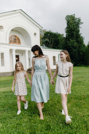 Relaxed happy mother and two little daughters outdoors in the park. Parenthood and child concept.