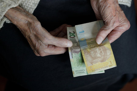 Womens hands hold several Ukrainian hryvnias. Pension, poverty, social problems and the topic of old...