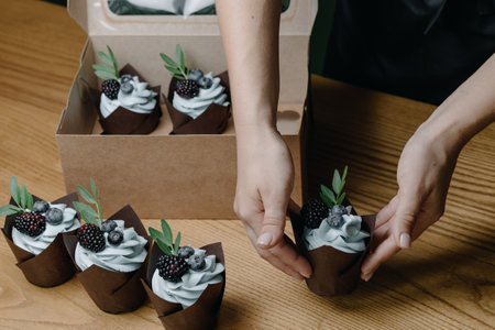 Close-up of female hands placing cupcake on table. Packaging of cupcakesの写真素材