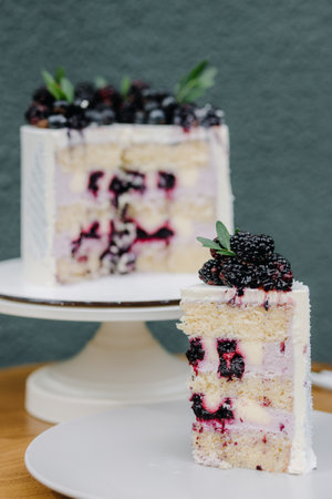 A piece of cut cake with berries on a white plate on a blurred cake background.の写真素材