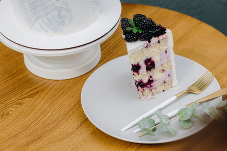 A piece of cake with berries on a white plate with utensils on the tableの写真素材