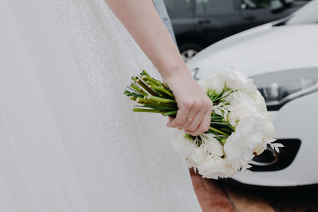 A wedding bouquet of white roses in the hand of the bride on the streetの写真素材