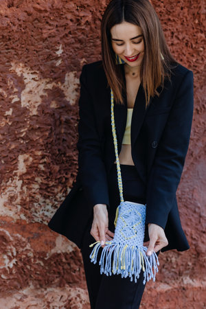 Street portrait of a young brunette woman in a black suit looking at a macrame phone case in Ukrainian colorsの写真素材