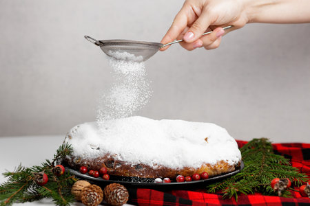 A womans hand sprinkles powder through a sieve on a German Christmas stollenの写真素材