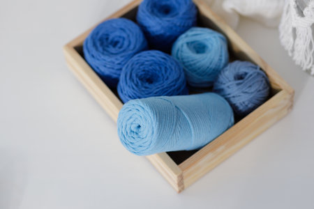 Balls of blue and light blue cotton macrame ropes in a wooden box on a white table