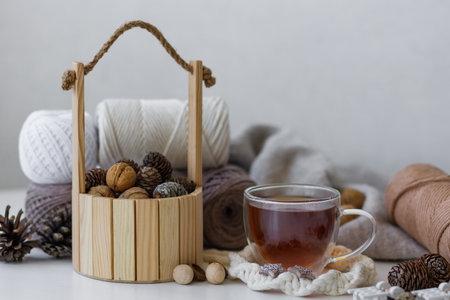 Homemade winter composition with cup of black tea, knitted sweater, wooden bucket with nuts and pine...