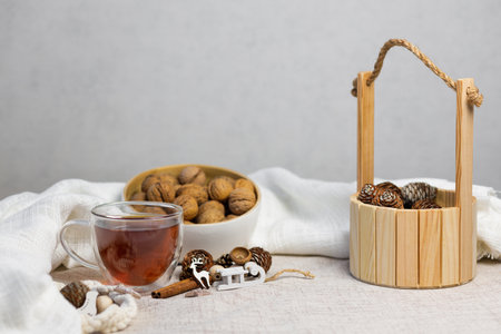 Homemade winter composition with cup of black tea, white cloth, wooden bucket with nuts and pine...