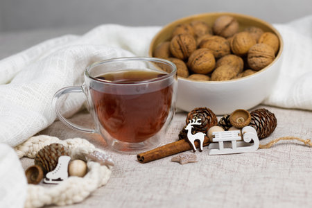 Cup of tea and nuts, cones, cinnamon sticks, small sled and deer, white cloth. Christmas, winter concept. Side view lay flat.の写真素材