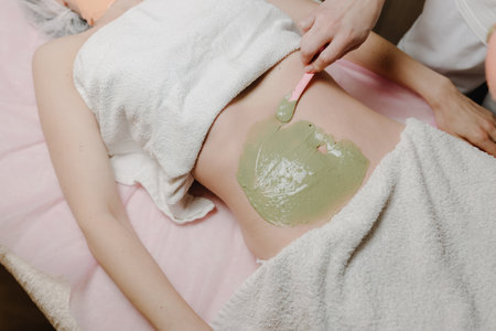 The process of applying a filling alginal mask to the abdomen of a young European woman. Abdominal rejuvenation procedure. Skin care in a beauty salonの写真素材