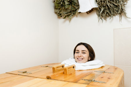 Face of a smiling young European brunette in a cedar barrel smiling and looking at the camera. Salon procedures.の写真素材