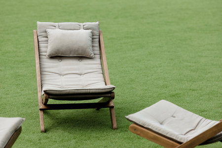 A tranquil scene featuring a comfortable deckchair placed on a lush green lawn, with plenty of copy space for your design or text. The perfect place to relax and unwind on a sunny day.の写真素材