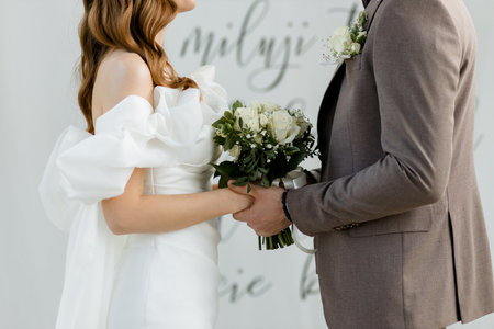 Close-up shot of a newlywed couple holding hands in a beautiful registry office during their heartwarming wedding ceremony, symbolizing love, commitment, and the start of a new journey togetherの写真素材