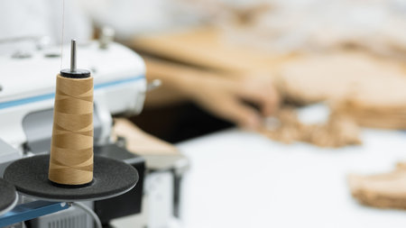 A close-up of a brown sewing thread skein resting on a spool, with a blurred fabric background in the backdrop. The image showcases the tools used in sewing and textile work.の写真素材