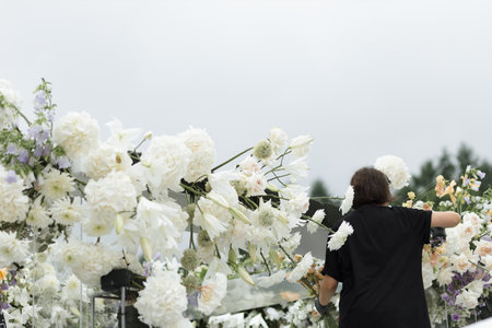 A professional wedding decorator is skillfully arranging fresh flowers on an outdoor arch to create a stunning and elegant backdrop for a romantic and beautiful wedding ceremony in an outdoor setting.の写真素材