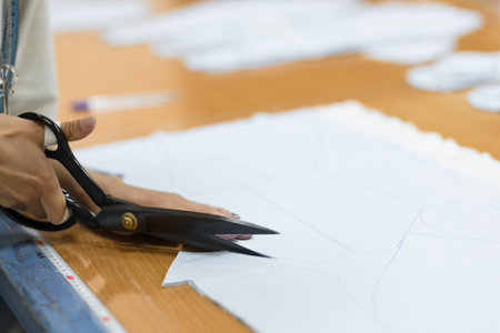 Close-up of a woman's hands cutting fabric for sewing with a pair of sharp scissors. The focused hands show precision and expertise in dressmaking and textile crafting.の写真素材
