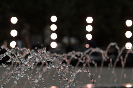 A captivating view of water droplets mid-air, illuminated by the soft glow of city lights in the background.の写真素材
