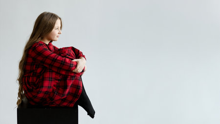 A person wearing a red plaid shirt and black pants, sitting on a black surface against a white background.の写真素材