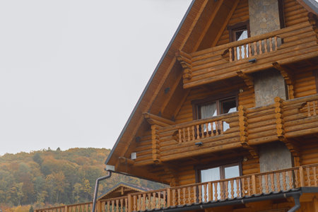 A cozy wooden cabin with detailed craftsmanship, nestled against a backdrop of lush greenery and hills.の写真素材