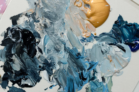 A close-up of mixed paint strokes, showcasing a blend of blue, gold, and white colors creating an abstract art piece.の写真素材