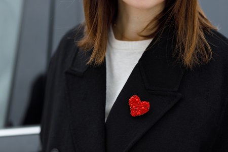 A close-up of a woman wearing a black coat adorned with a sparkling red heart-shaped brooch. The...