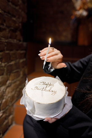 A woman holds a beautifully decorated birthday cake with Happy Birthday written on it, lighting a candle to celebrate the special occasionの写真素材