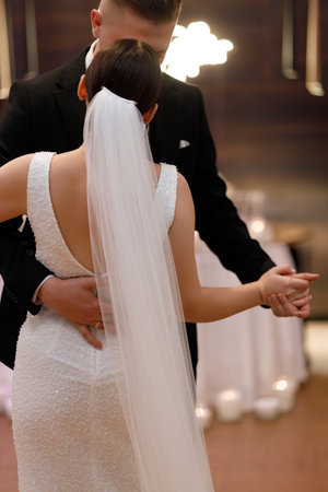 A newlywed couple shares their first dance, enveloped in each others arms. The brides elegant white dress adorned with intricate detailing glistens under the soft, ambient lighting of the venue, capturing a moment of pure bliss and unityの写真素材