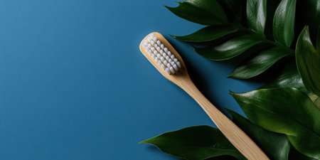 A bamboo toothbrush with natural bristles rests elegantly on lush green leaves against a striking blue backdrop, highlighting a commitment to sustainable living and eco-conscious choices.の素材