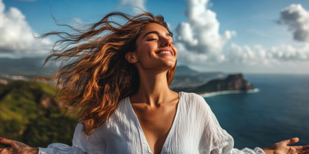 A woman with flowing hair stands on a hill, arms outstretched, soaking in the stunning coastal view. The bright blue sky and gentle breeze evoke a feeling of pure freedom and relaxation.の素材